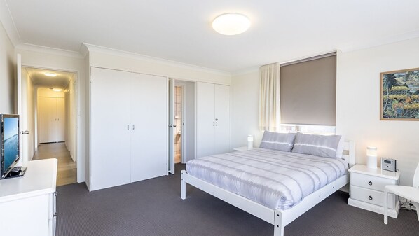Une chambre à coucher comprenant un lit, des tables de chevet, une armoire, un téléviseur et un tableau accroché au mur.
