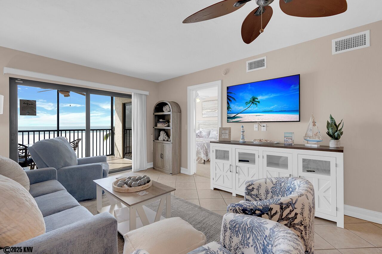Een ruime woonkamer met een grote televisie, comfortabele zithoek en uitzicht op zee door grote ramen.