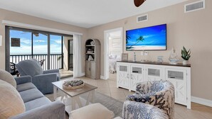 Un salón amplio con un televisor grande, asientos cómodos y vista al océano a través de ventanas panorámicas.