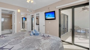 Un dormitorio con cama, televisión y puerta corrediza de vidrio que da a un balcón.