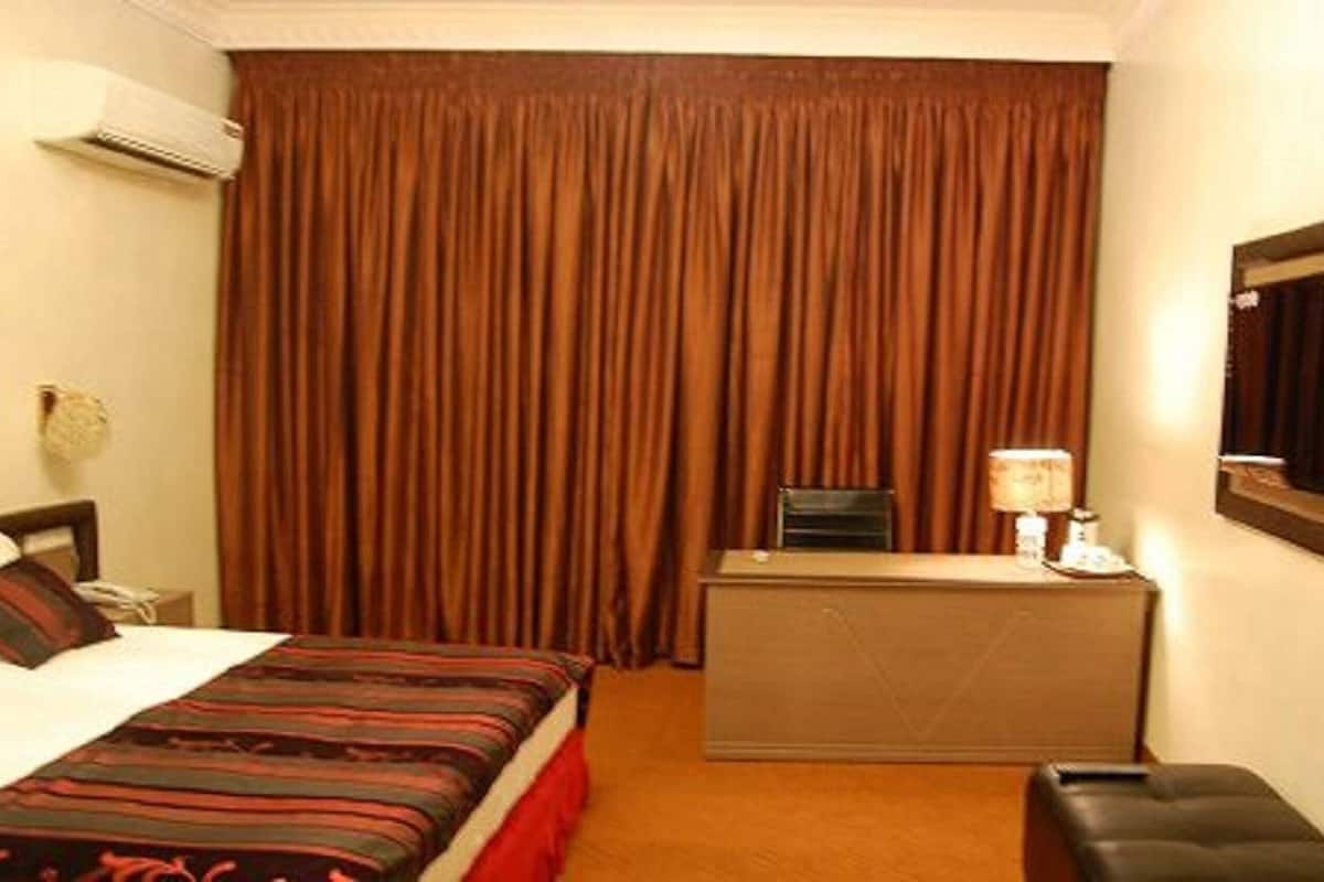 Hotelkamer met een bed, bureau, stoel, airconditioning en een groot raam met gordijnen.