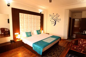 A hotel room with a large bed, wooden flooring, a mirror, a desk, and a chair. - Hotel Vatika (Palampur)