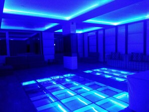 A room with a blue-lit floor and a seating area with a sofa and armchairs. - Hotel Vatika (Palampur)
