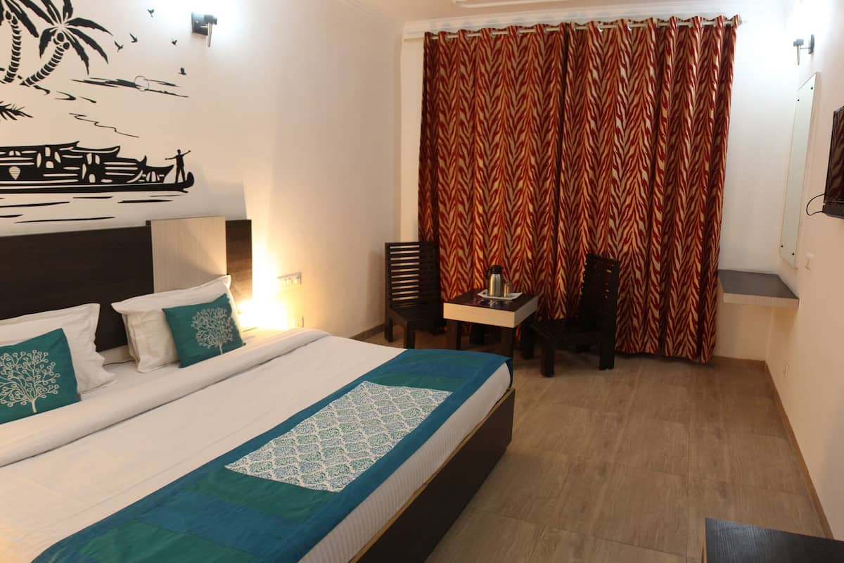 Habitación de hotel con cama, escritorio, silla, espejo y un mural tropical en la pared.