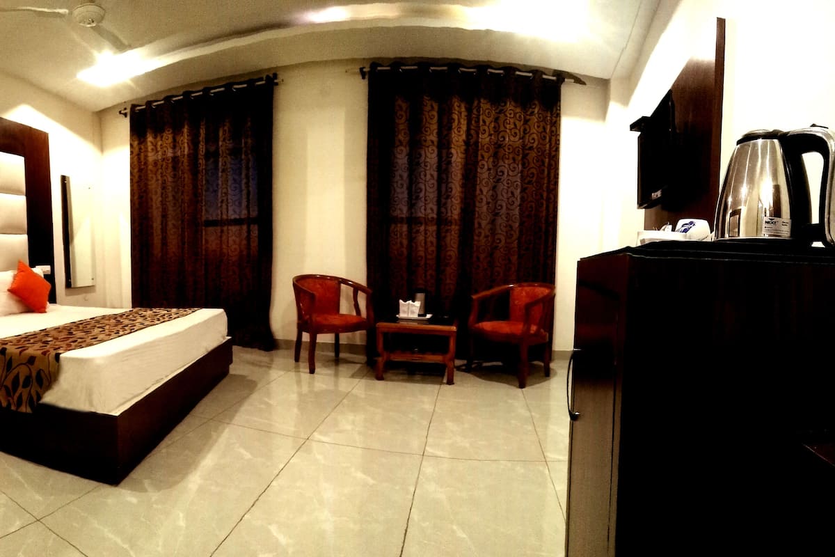 Una habitación de hotel con una cama grande, una mesita, dos sillas y una cafetera.