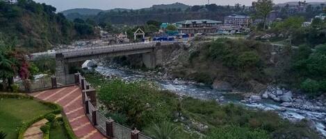 A bridge over a river with a pathway leading to a building with a green roof.
