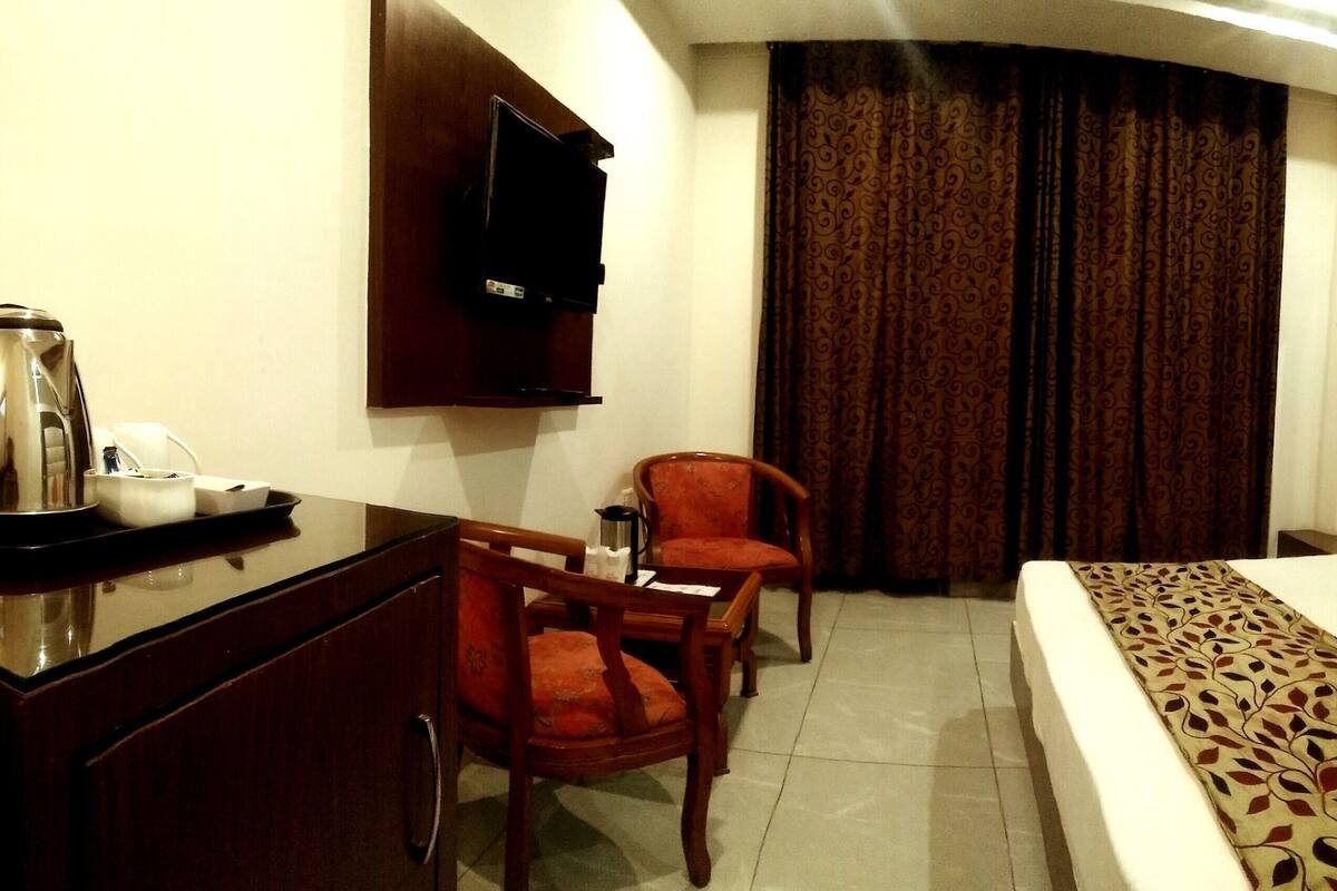 Una habitación de hotel con una cama, un escritorio con silla, un televisor y una ventana con cortinas.