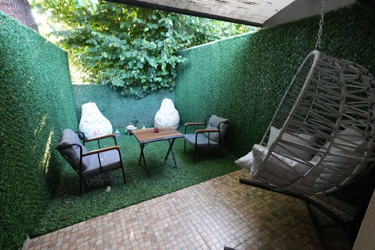 A patio with a hanging chair, two cushioned chairs, and a small table.