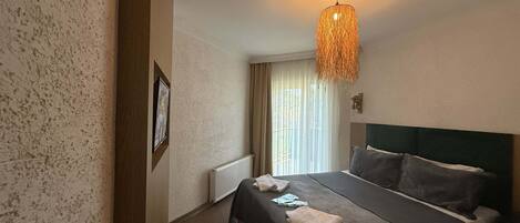 Une chambre d’hôtel avec un lit, un radiateur, un luminaire suspendu et une fenêtre avec des rideaux.
