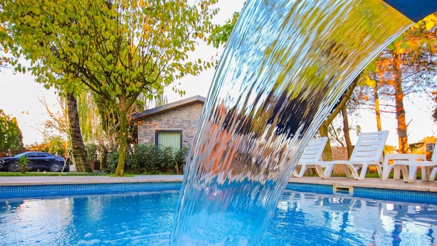A swimming pool with a water feature, surrounded by lounge chairs and trees. - Alex Village Life (Kartepe)
