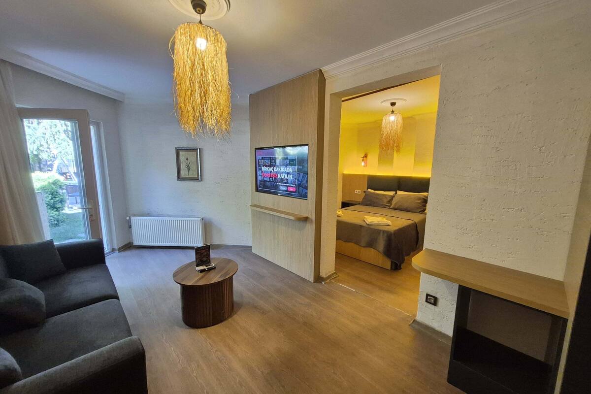 A modern living room with a sofa, a TV, a fireplace, and a bed in the background.