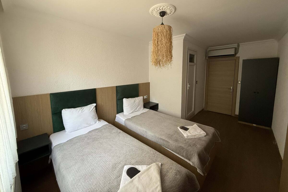 A hotel room with two single beds, a ceiling fan, a wardrobe, and a door.