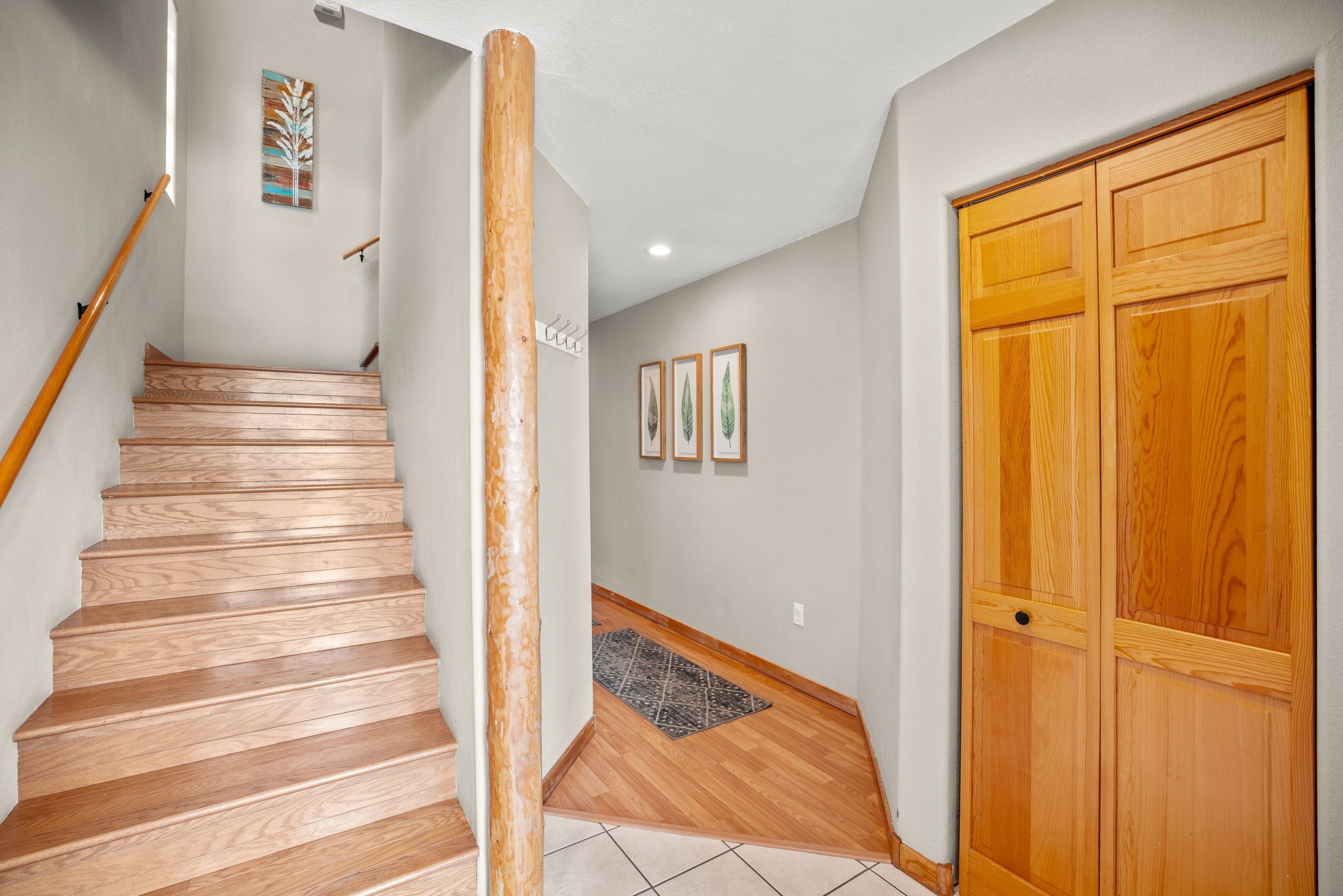 A wooden staircase leading to a landing with a rug and framed pictures on the wall.