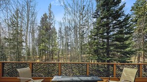An outdoor deck with a table and chairs, surrounded by a wooden railing and a view of tall trees. - Cutty Sark Court #1 3br 2.5ba Mountain Views 3 Bedroom Townhouse by RedAwning (Silverthorne)