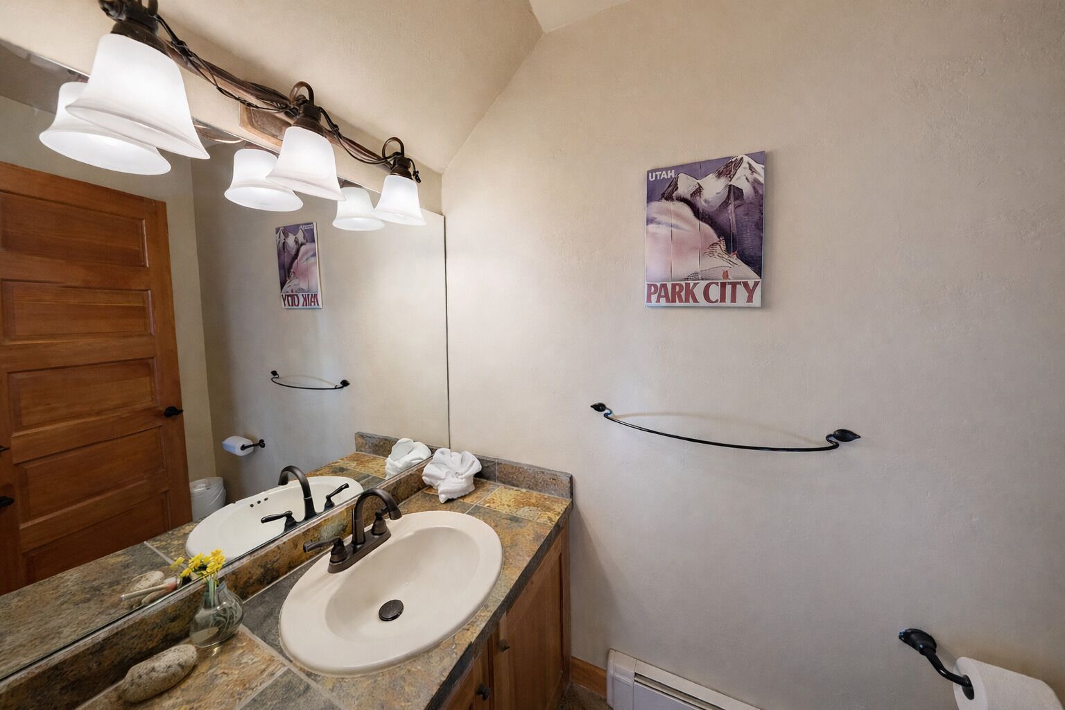 A bathroom with a sink, mirror, towel rack, and a poster of a mountain labeled "Park City."