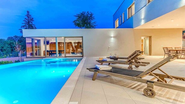 Ein moderner Außenpoolbereich mit Liegestühlen und einem verglasten Spa-Bereich.