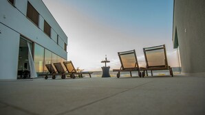 Ein modernes Gebäude mit großen Fenstern, Außenbereich mit Liegestühlen und Blick aufs Meer.
