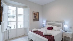 A bedroom with a large bed, two bedside tables, a window with shutters, and a painting on the wall. - Cadiz Wonderland apartment (Cádiz)