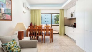 A modern apartment with a dining area, kitchenette, and a large window with curtains.