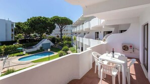 A balcony with a pool, white furniture, and a view of a residential area.