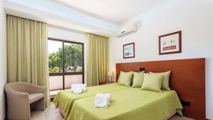 A hotel room with two beds, a chair, and a large window.