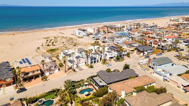 Vista aérea de una zona residencial costera con casas, una playa y un cielo azul despejado.
