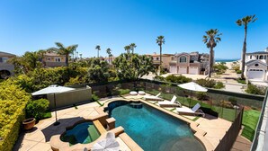 Una piscina con sillas de descanso y sombrillas, rodeada de palmeras y casas.