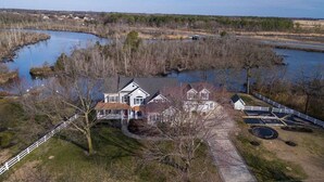 A large house with a porch, a fenced yard, and a river in the background.