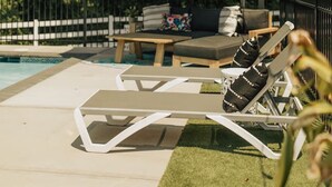 A poolside area with lounge chairs, a table, and a blue umbrella.