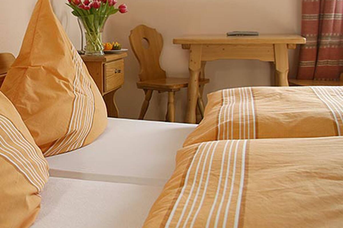 A hotel room with a bed, a wooden nightstand, a small table, and a chair.