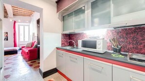 Cozinha compacta com micro-ondas, pia e armários. Um sofá vermelho visível na área de estar adjacente.