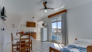 A compact hotel room with a bed, a dining table with chairs, a kitchenette, and a balcony with a view. - Marazul Apart Hotel 2 (Florianópolis)