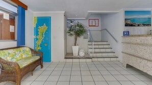 A reception area with a wicker sofa, a map on the wall, a staircase, and a plant. - Marazul Apart Hotel 2 (Florianópolis)