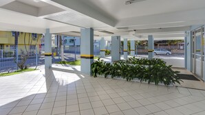 A covered outdoor area with tiled flooring, blue pillars with yellow stripes, and a row of green plants. - Marazul Apart Hotel 2 (Florianópolis)