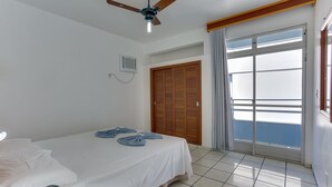 A hotel room with a bed, ceiling fan, air conditioning unit, and a view of the sea through a large window. - Marazul Apart Hotel 2 (Florianópolis)
