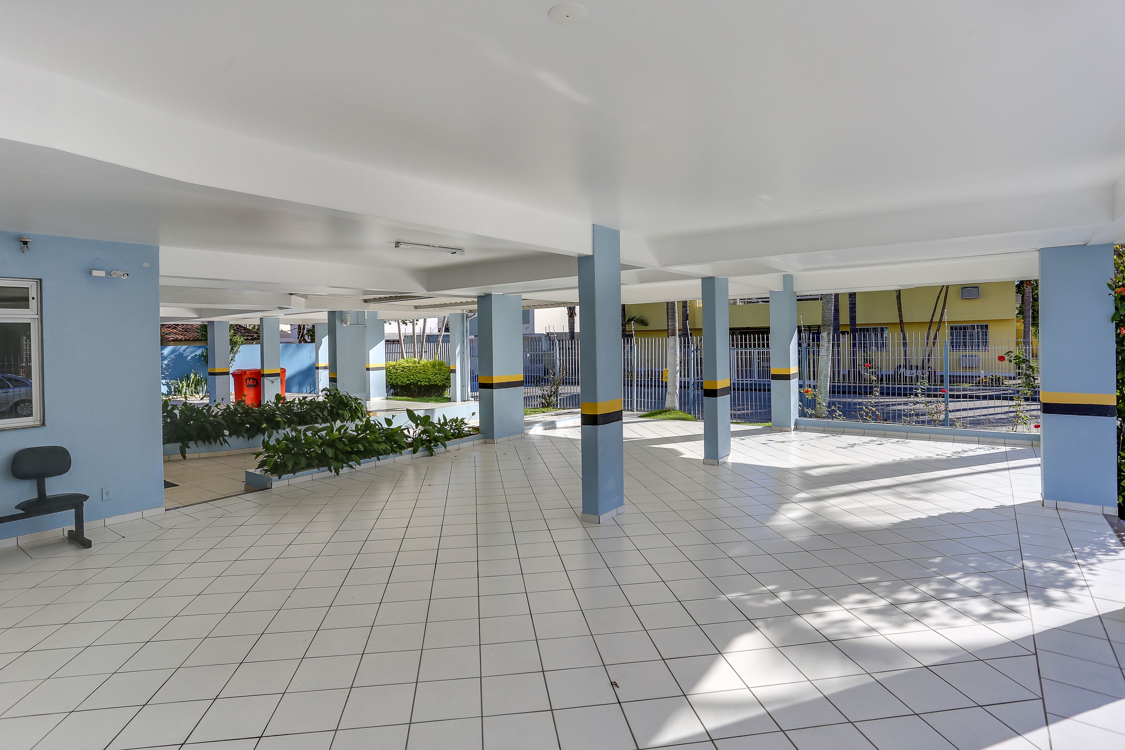 A spacious indoor area with tiled flooring, blue pillars, and a bench.