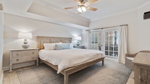 Une chambre à coucher avec un lit en bois, deux tables de chevet avec des lampes, un ventilateur de plafond et une grande fenêtre avec des stores.