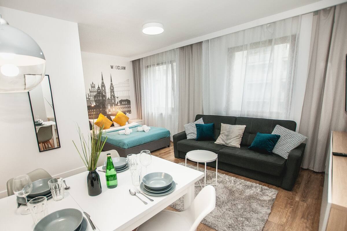 A modern living room with a sofa, dining table, and a cityscape mural on the wall.