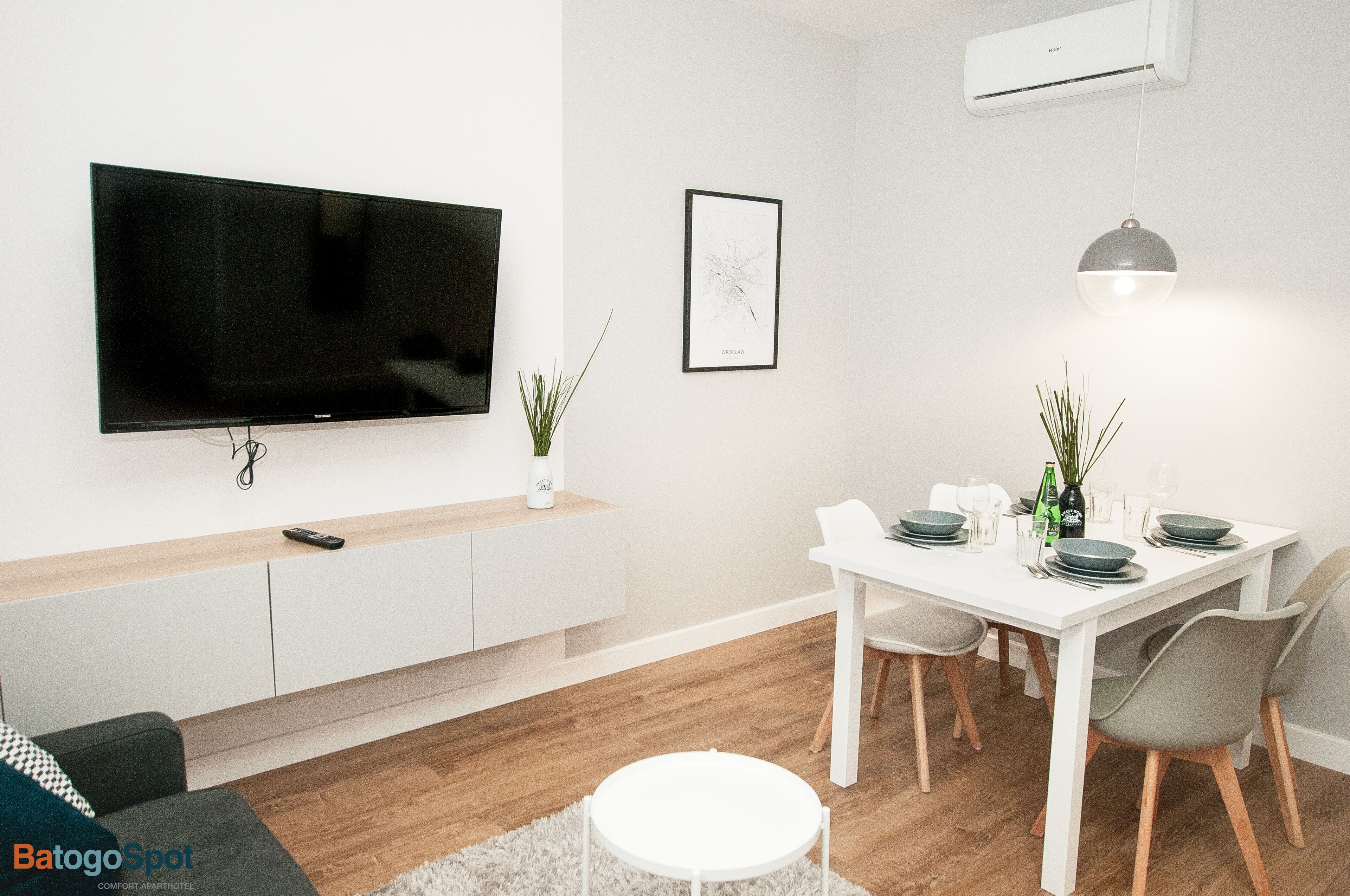 A modern living room with a flat-screen TV, a dining table set for four, and a white sofa.