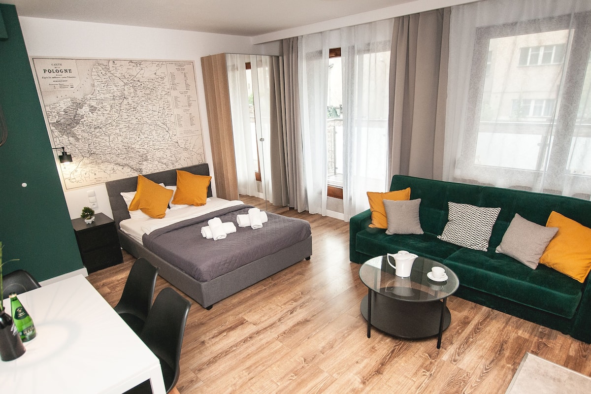 A modern hotel room with a bed, a green sofa, a coffee table, and a map on the wall.