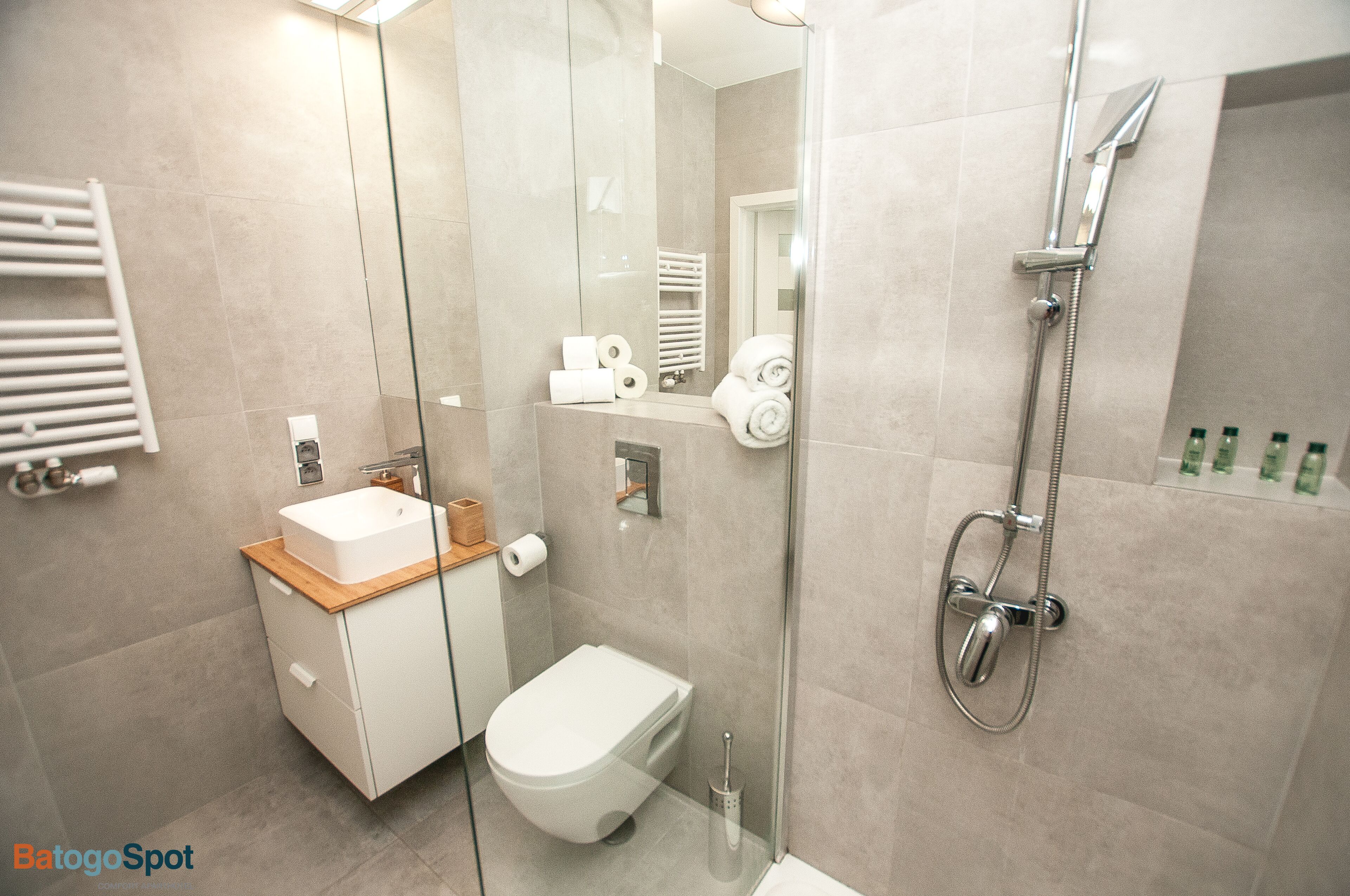A modern bathroom with a glass-enclosed shower, a white toilet, and a sink with a wooden countertop.