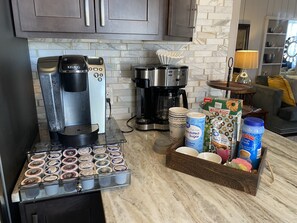 A kitchen with a Keurig coffee maker, a coffee pot, and a coffee machine. There are cups and a box of Krisp Kreme donuts.