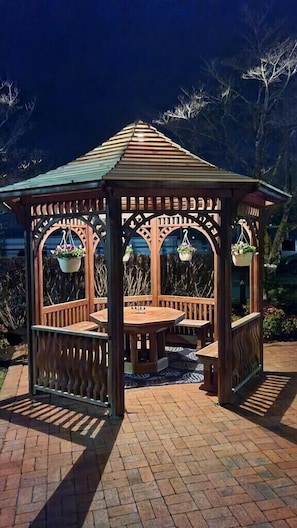 A wooden gazebo with a tiled roof, benches, and hanging planters.