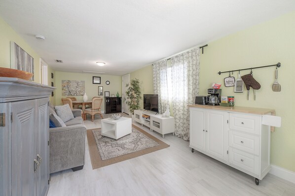 A living room with a sofa, coffee table, TV, and a kitchen area with a countertop and cabinets.