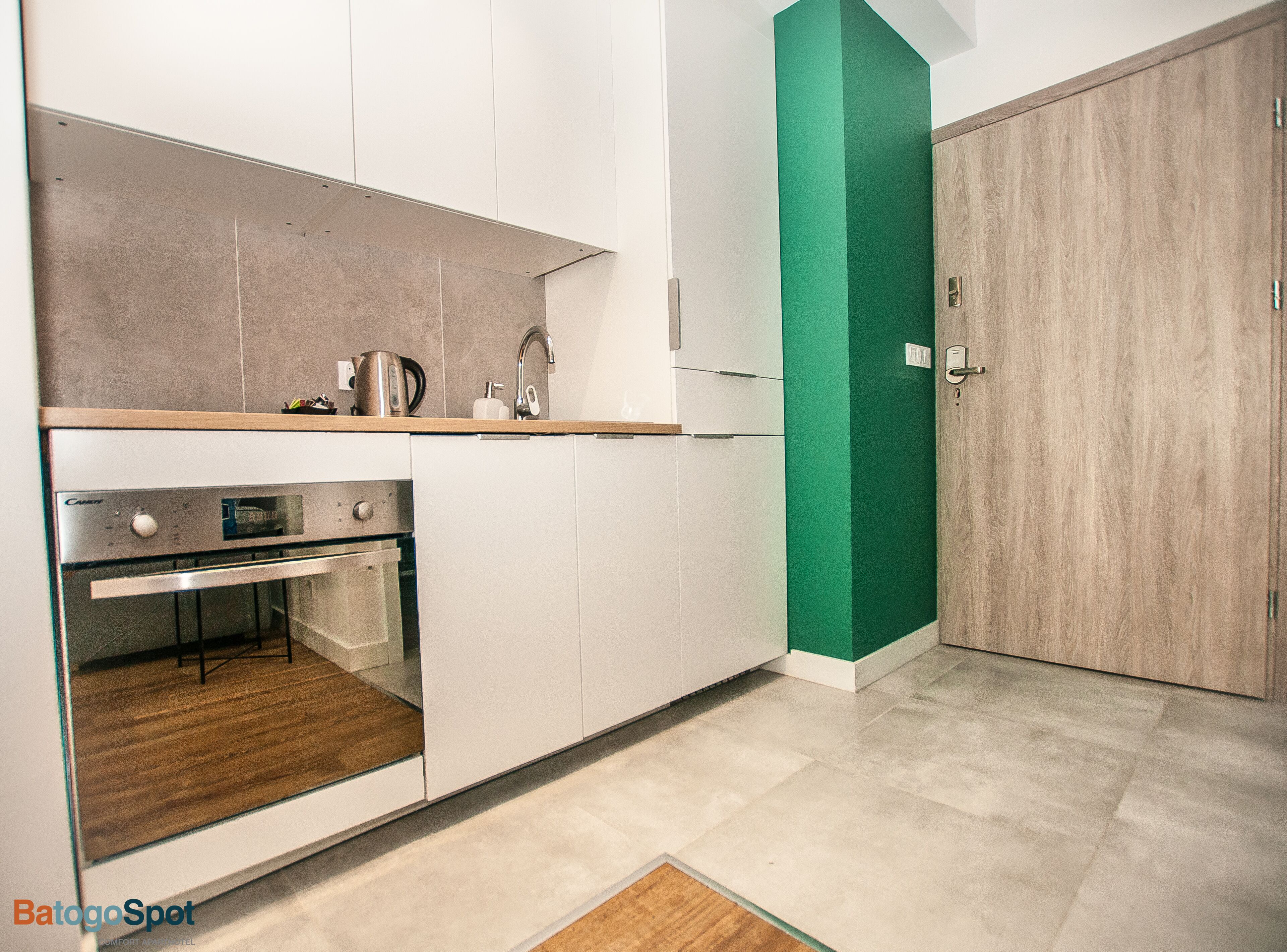 A modern kitchen with white cabinets, a built-in oven, and a green accent wall.