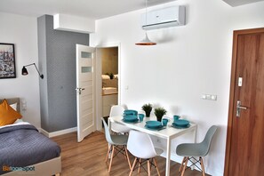 A modern hotel room with a bed, a desk with chairs, a dining table with blue plates, and an air conditioning unit. - BatogoSpot Tumski 2 (Wroclaw)
