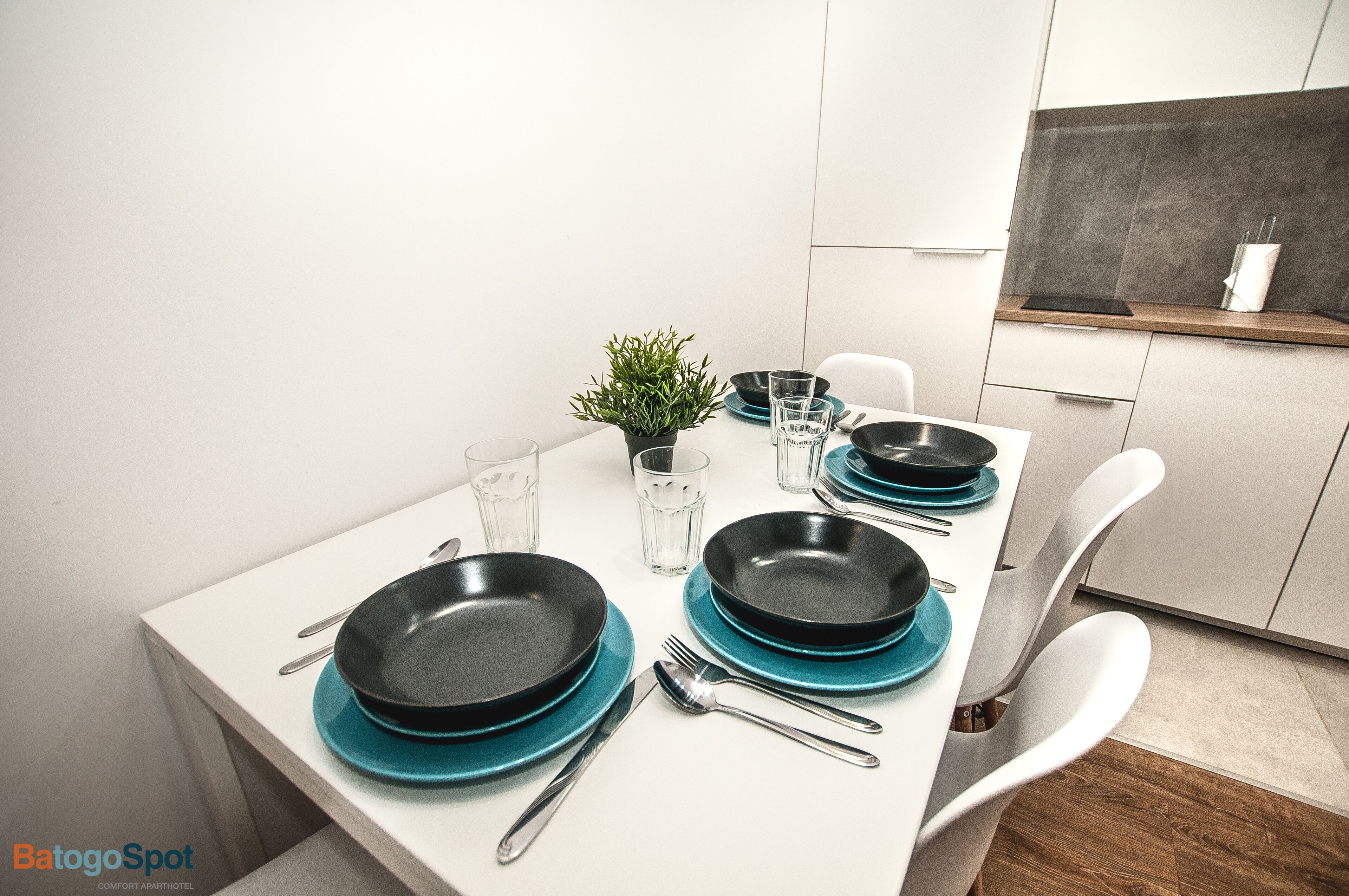 A modern dining table set with black and teal plates, silverware, and clear glasses, with a small potted plant in the center.