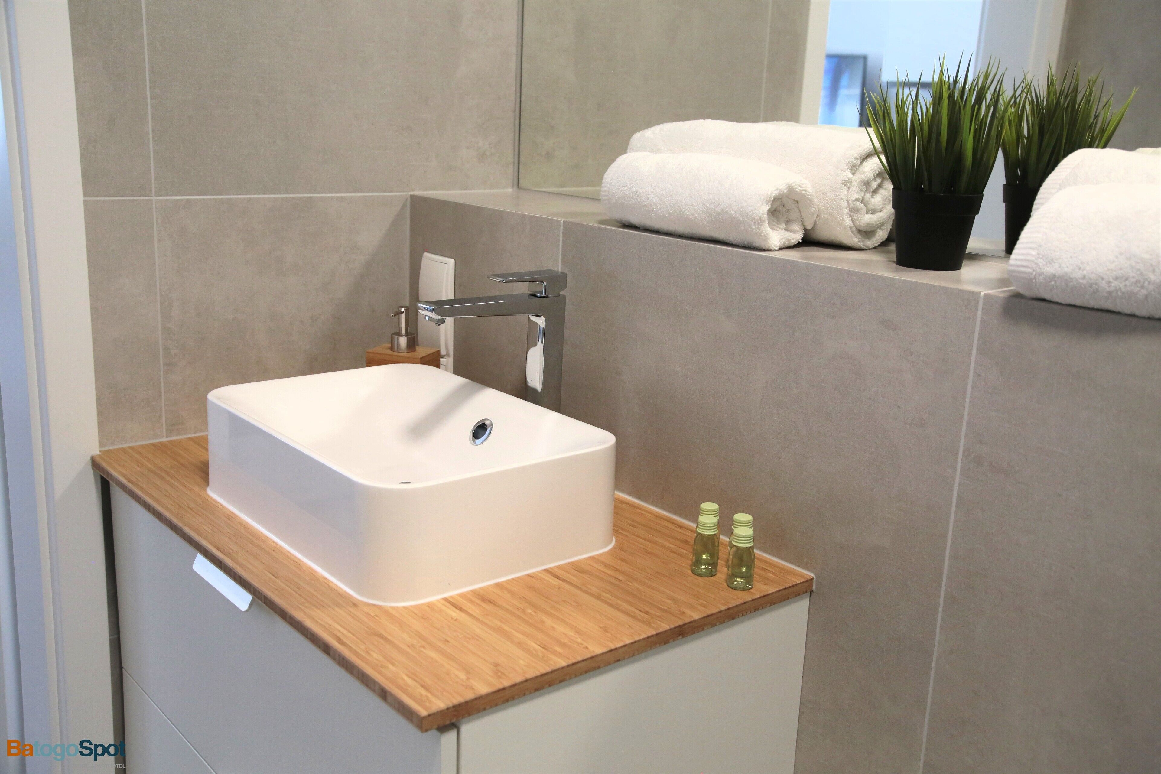 A modern bathroom with a white sink, wooden countertop, and two potted plants.