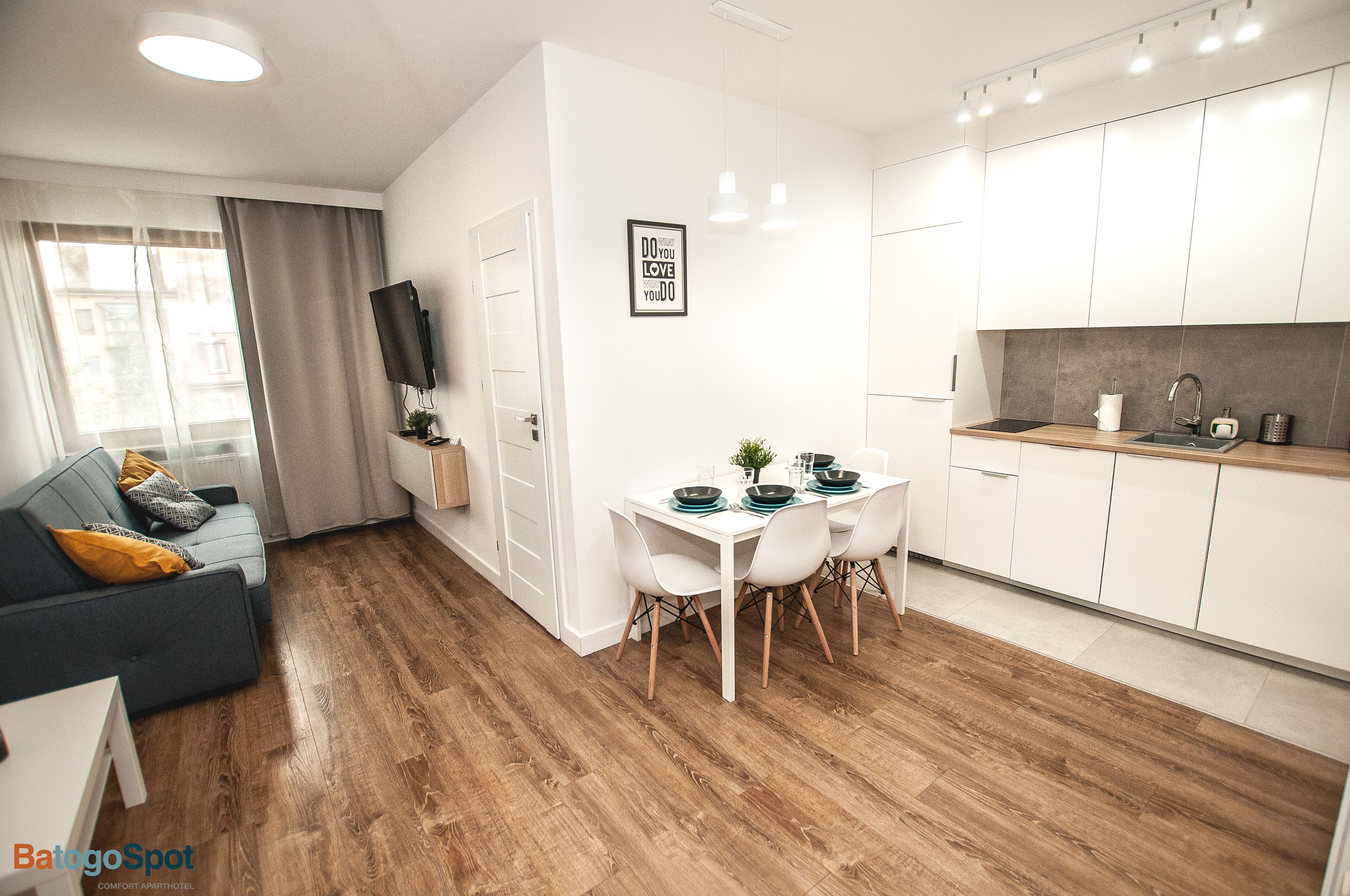 A modern apartment with a dining area, kitchenette, and a living room with a sofa and TV.