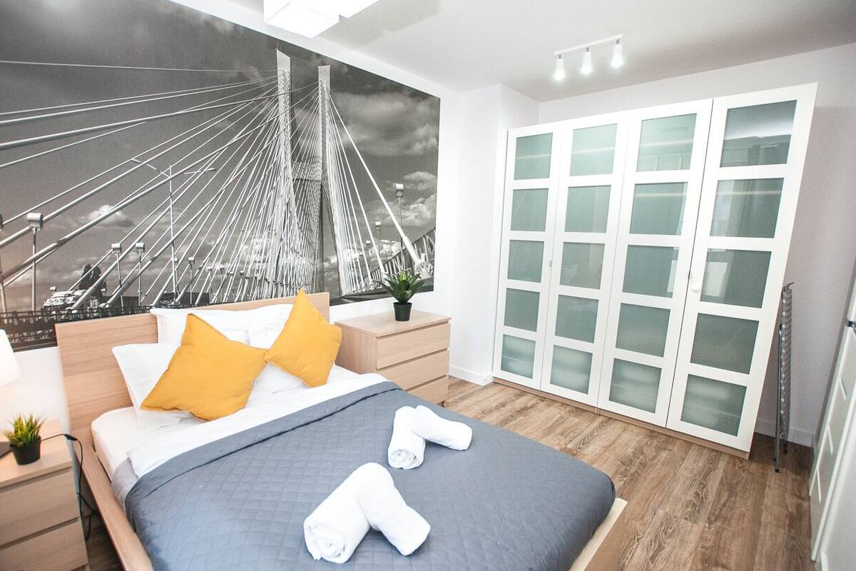 Une chambre d’hôtel moderne avec un grand lit, une table de chevet avec une lampe, une plante et une armoire aux portes en verre dépoli.